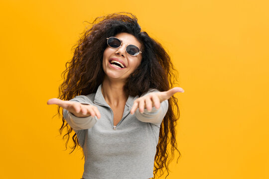 Come To Me. Excited Latin lady Extending Hands At Camera, Holding Big Invisible Oblect, Arab Woman Offering Hugs Or Wants To Grab Something, Standing Isolated Over Yellow Background, Copy Space