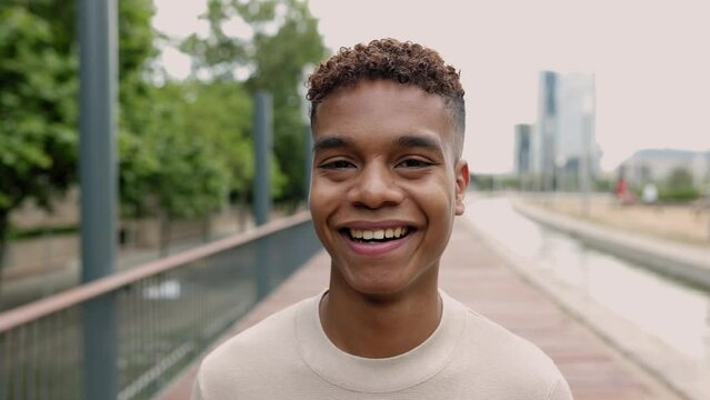 Face portrait of happy confident young adult hispanic latin teenager boy walking outdoor while smiling at camera. Slow motion front view high quality 4k footage