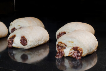 Many mini puff pastry buns with chocolate filling baking and rising on tray in electric oven - close up view. Homemade bakery, cooking, pastry and food concept