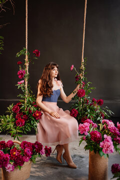 a beautiful young woman in a dress sits on a swing in peony flowers. 