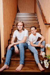 two brothers of a teenager in white T-shirts and jeans on a wooden staircase 