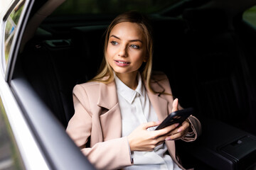 Beautiful business woman in car with phone on back seat