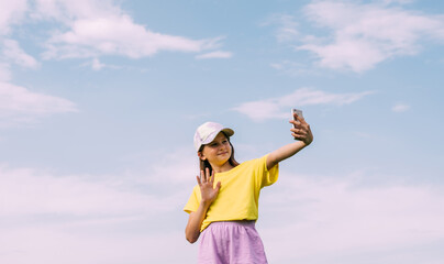 Fototapeta na wymiar A preteen girl takes a selfie on a mobile phone against a blue sky. Horizontal frame, copy space