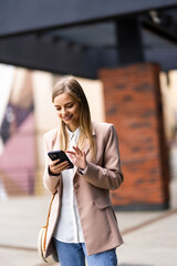 Obraz premium Portrait of young business woman talking on the phone while standing outside office buildings. Business and success concept.