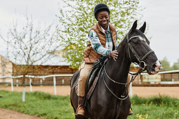 Portrait of smiling black woman riding horse in outdoor country ranch and stroking gently, copy...