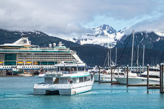06-24_2022 Seward Alaska USA Tour boat backing out of mooring space on docks with Alaskan Cruise ship and misty mountains with snow in background