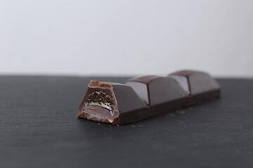 A piece of chocolate with jelly fruit filling lies on a gray background with a place for copyspace text. The day is idle. Chocolate Day holiday. The benefits and harms of sweets e. dental health
