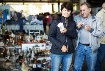 Adult happy man and his wife are visiting market of old things and looking collectible outdoors.