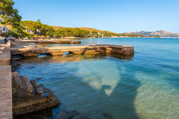 Obraz premium The beach and promenade with the piers of Port de Pollença in the evening at sunset.