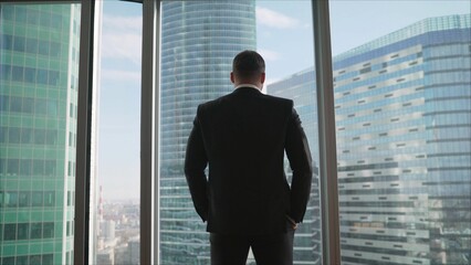 Looking out of the Window. Window Has Panoramic View on Big City Business District. The businessman walks confidently to the window.