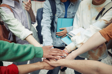 Group of intercultural teenage students in casualwear making pile of hands while standing in circle...