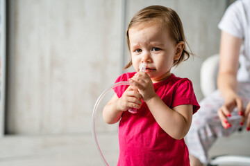 One girl little caucasian child toddler standing with nose snot sucker nasal aspirator looking to the camera copy space