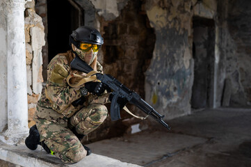 Fototapeta premium Portrait of a woman in a helmet and goggles with a machine gun in her hands. A female soldier in a camouflage uniform holds a weapon.