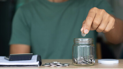 Fototapeta na wymiar Businessman putting coins in a glass jar with a calculator and notebook. the concept of saving money for the future, Business, finance, accounting, investment, and financial planning.