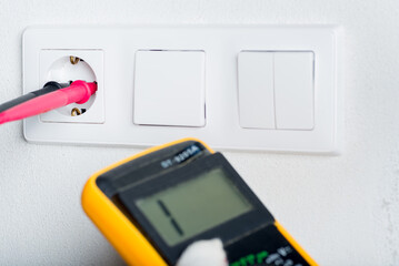 The electrician measures the electrical socket with a multimeter. European high voltage 230V standard. - 516237994