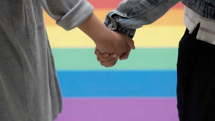 Closeup young adult queer transgender lover asia two people hold hand with colorful stripes flag. Proud of LGBT or LGBTQIA partner culture hug love sign in bisexual festival march day at city street.