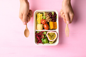 Fresh vegetables salad in biodegradable bowl with hand on pink background, Healthy vegan food