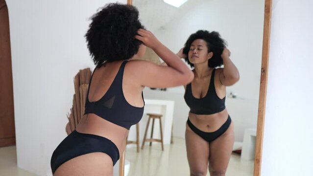 Multicultural plus size woman in lingerie looking at her body in the mirror. Black woman struggles with obesity and overweight, wants to lose weight and be slim Woman body positive without criticism