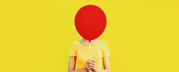 Portrait of funny woman covering her head with red balloon on yellow background