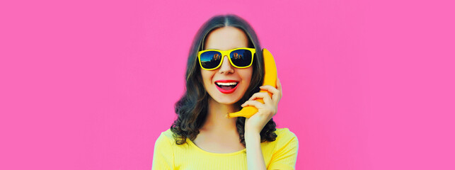 Portrait close up of funny young woman calling on banana phone on pink background