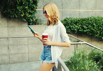 Beautiful smiling young woman with smartphone and coffee cup in the city