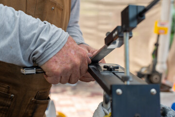 A man using a fixed angle knife sharpener kitchen tools at a farmer's market to sharpen knives for customers. The stainless steel kit has a long narrow holder for water stones of various grits. 