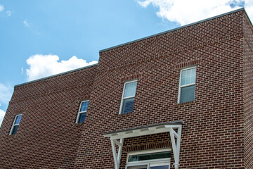 The exterior of a tall red and brown colored brick building with multiple double hung windows with black trim. The vintage apartment building has a tree covered in pink flowers in the foreground.