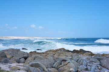 Fototapeta na wymiar Rocks in the ocean under a blue sky with copy space. Beautiful landscape of beach waves splashing against boulders or big stones in the sea at a popular summer location in Cape Town, South Africa