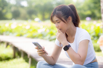 Happiness young asian woman sitting and using smart phone on social network online in the park, girl relaxation using smartphone and video call on summer in the garden, communication concept.