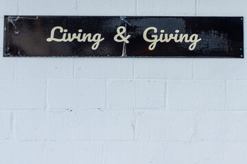 An exterior brick wall was painted white. Along the top of the wall is a narrow black banner with the words living and giving in white script. The building has a rough texture and groves. 