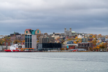 Naklejka premium Daytime downtown St. John's, Newfoundland, under blue skies. Multiple supply vessels docked to support the offshore gas and oil industry. The cityscape has colorful buildings, houses, and churches.