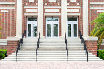 Concrete steps lead to a red double door of a historic building. The wall of the building is made...