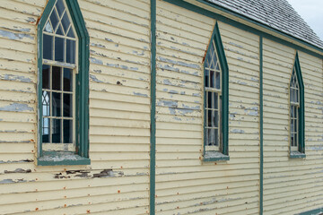 The exterior wall of a religious building with pale yellow colored narrow horizontal clapboard...