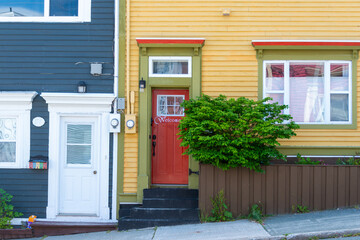 Two colorful entrances to adjoined or townhouses. One building is blue with a white door the other is yellow with a red door and green and red decorative trim. The sidewalk is on a slope.