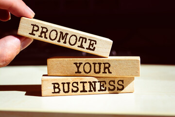 Promote your business symbol. Businessman hand. Wooden blocks with words 'Promote your business'.
