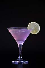 Cosmopolitan, alcoholic cocktail with ice and in a tall glass with a slice of lemon on a black background.