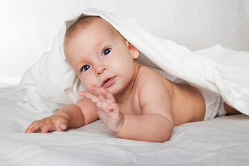 A half-year-old cute baby in a diaper and a towel lies on his stomach and looks cheerfully at the camera