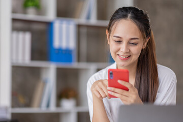 Happy Excited Asian young entrepreneur business woman using phone and laptop sitting on a desk officer in the day at the office