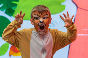 Lovely kid with paintings on his face and lion costume perform in a school festival  - obrazy, fototapety, plakaty