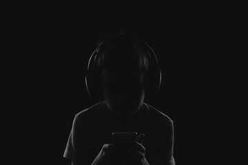 profile of a child in headphones looking at a phone in complete darkness