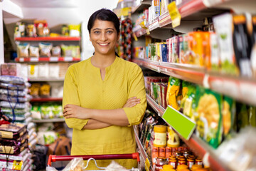 Happy woman owner with arms crossed at grocery aisle of supermarket