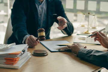 Male businessman and lawyer consulting with the client team on law, discussing and signing office contract with judge's scale and hammer on legal services concept table.
