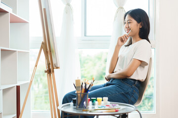 The art concept, Asian female artist sit front of canvas and thinking to create idea for artwork