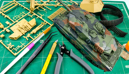 Top view of plastic model WW2 tank with part and tools such as paint brush,plier,cutter on cutting pad,Hobbie.
