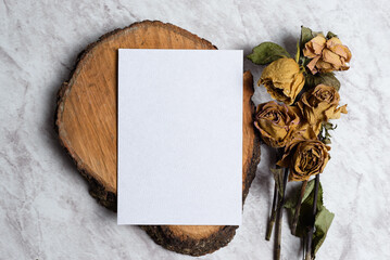 Blank card and wilted flowers on marble background. Concept of nostalgia, breakup, disappointment,...
