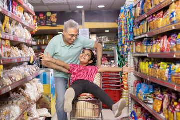 Grandfather is giving his granddaughter a ride in the shopping trolley while they're buying food in the supermarket