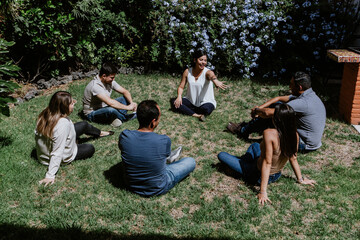 hispanic young people seated in circle on grass and participating at group therapy session in...