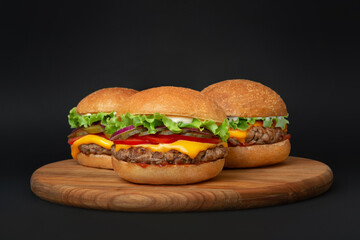 three burgers on a wooden board on a black background