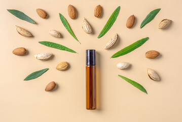 Bottle of cosmetic oil and nuts and leaves of almond on a beige background