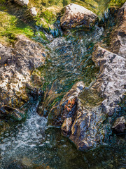 The water of a small torrent passes over the rocks of the riverbed. In some places, it flows gently as if caressing them, while elsewhere it runs impatiently, as if trying to smooth them.